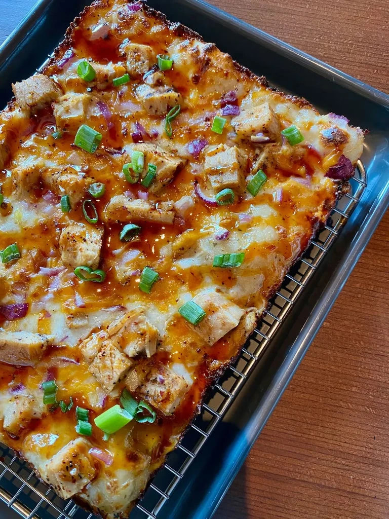 Rectangular chicken flatbread with melted cheese, BBQ sauce, and green onions.