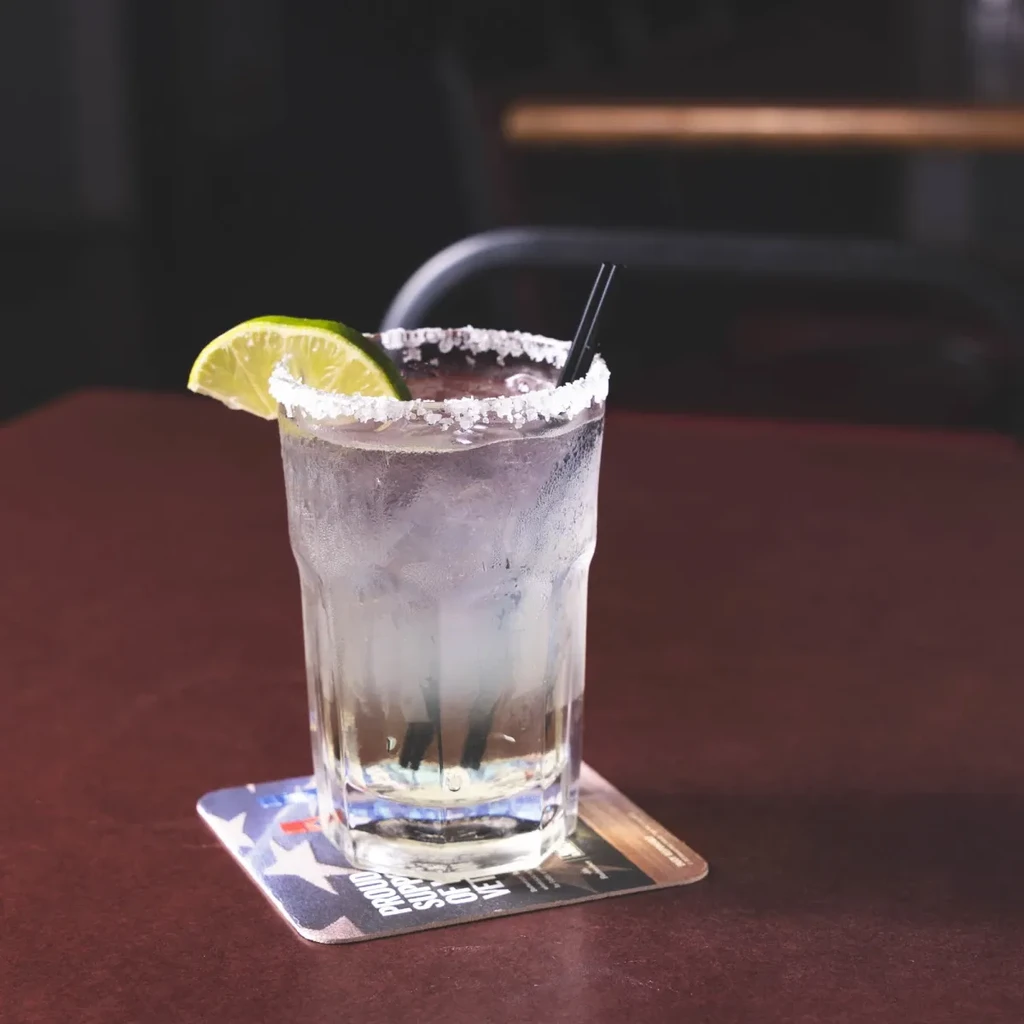 Cold clear cocktail in highball glass with lime, salted rim, and straws.