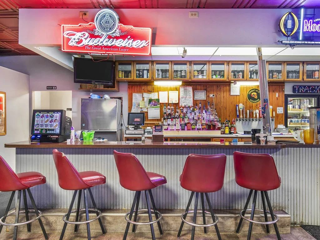 Restaurant bar with red stools, liquor, beer taps, and neon signs.