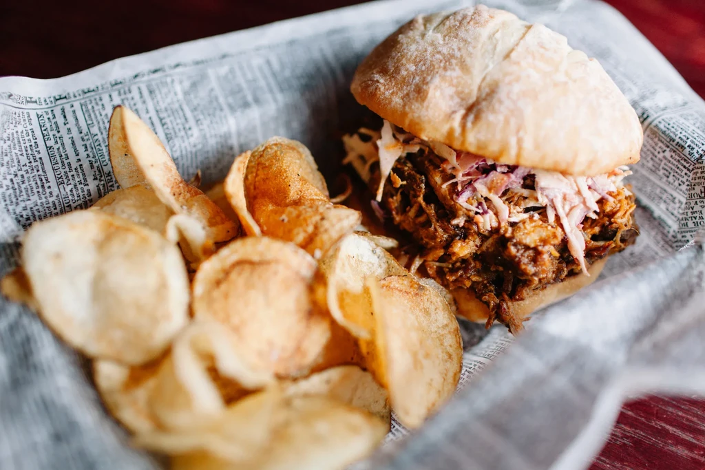 Pulled pork sandwich, coleslaw, and homemade chips in a newspaper basket.