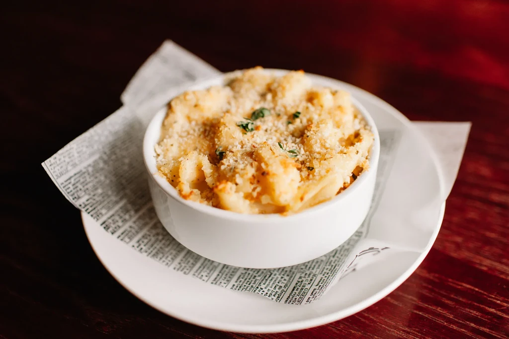 Baked pasta with crust, herbs, in white bowl on newspaper.