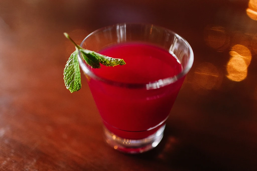 Vibrant red cocktail with mint garnish, dark wood, and warm bokeh.