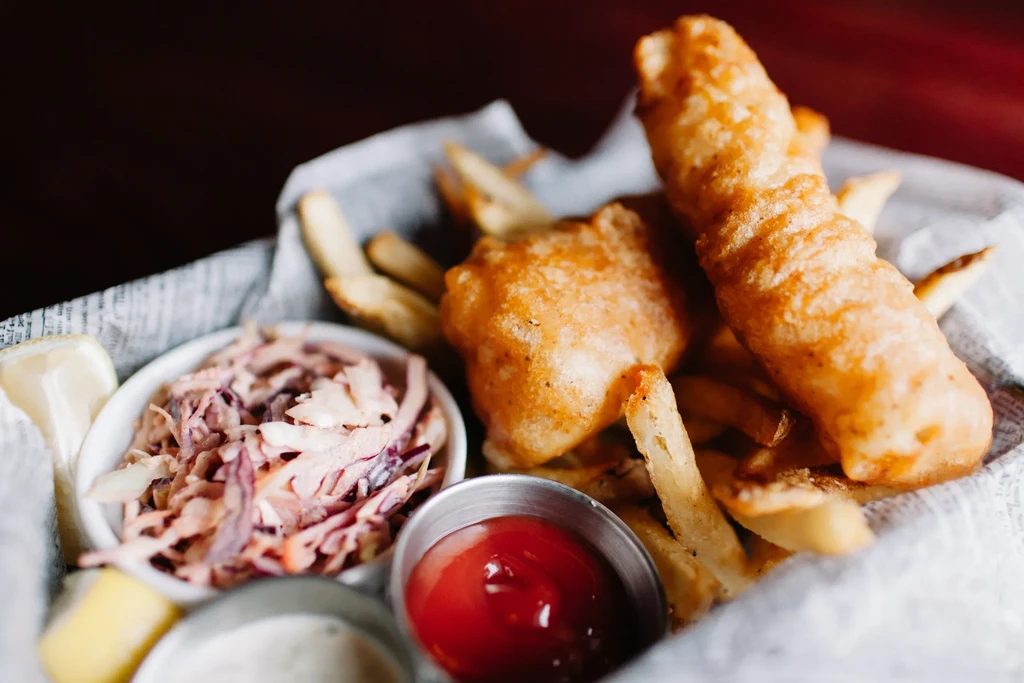 Golden fish and chips in a basket with coleslaw and sauces.
