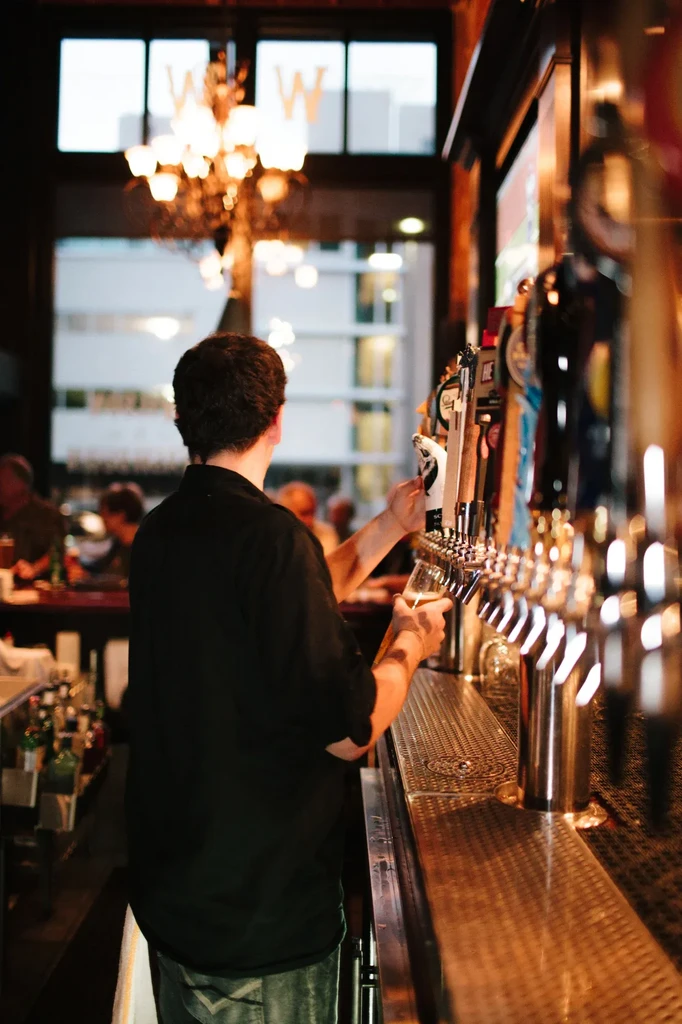 Bartender pouring a drink from taps at a bar.