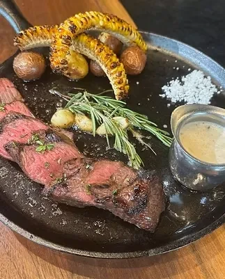 Medium-rare sliced steak, roasted potatoes, corn, and sauce in skillet.