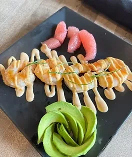 Shrimp with creamy sauce, avocado, and pink citrus on black plate.