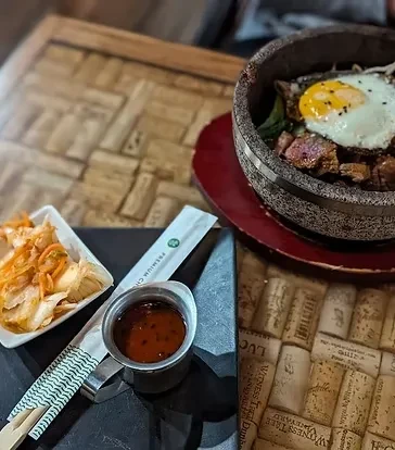 Overhead meal: seared meat, egg, kimchi, chopsticks on a wine cork table.