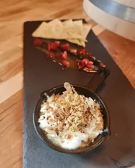 Creamy dish with crunchy topping, red fruit sauce, and crisps on slate.