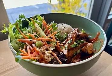 A teal ceramic bowl filled with colorful grain salad and protein.