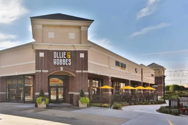 Restaurant 'Ollie & Hobbes' exterior with brick, stucco, patio, yellow umbrellas.