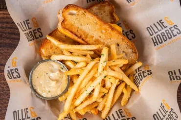 Two grilled cheese halves, fries, and sauce cup on branded paper.
