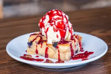 Bread pudding with baked berries, vanilla ice cream, and red berry sauce.