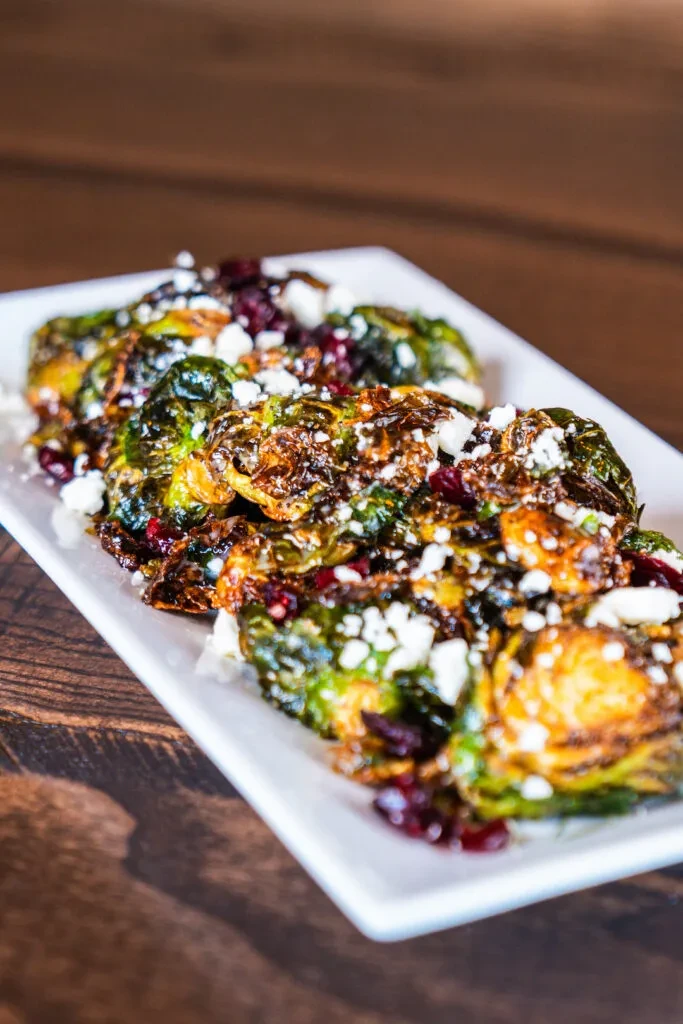 Caramelized Brussels sprouts with cheese crumbles and red fruit on a plate.