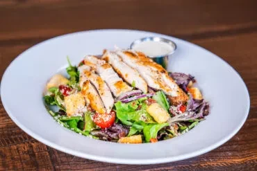 Grilled chicken salad with mixed greens, tomatoes, and dressing.