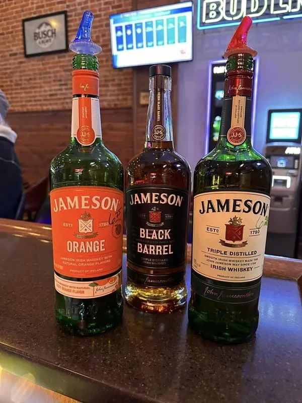 Three Jameson Orange, Black Barrel, and Triple Distilled bottles on a bar.