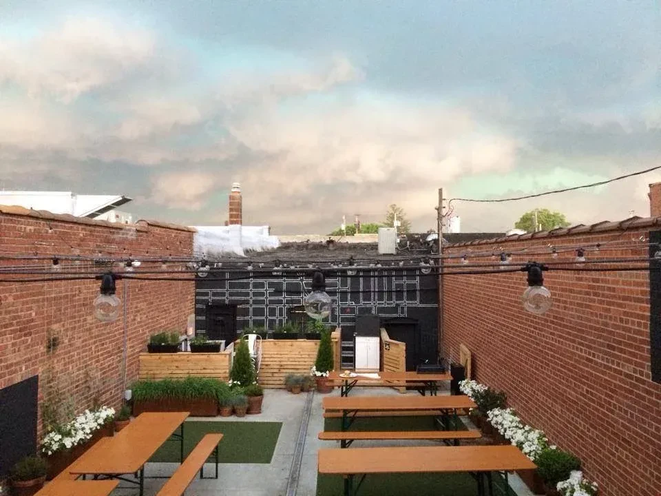 Outdoor patio with communal tables, string lights, and brick walls.