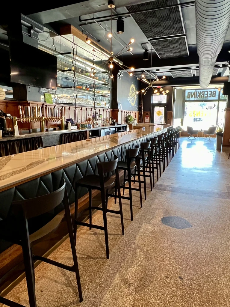 Long modern bar counter with many beer taps and dark stools.