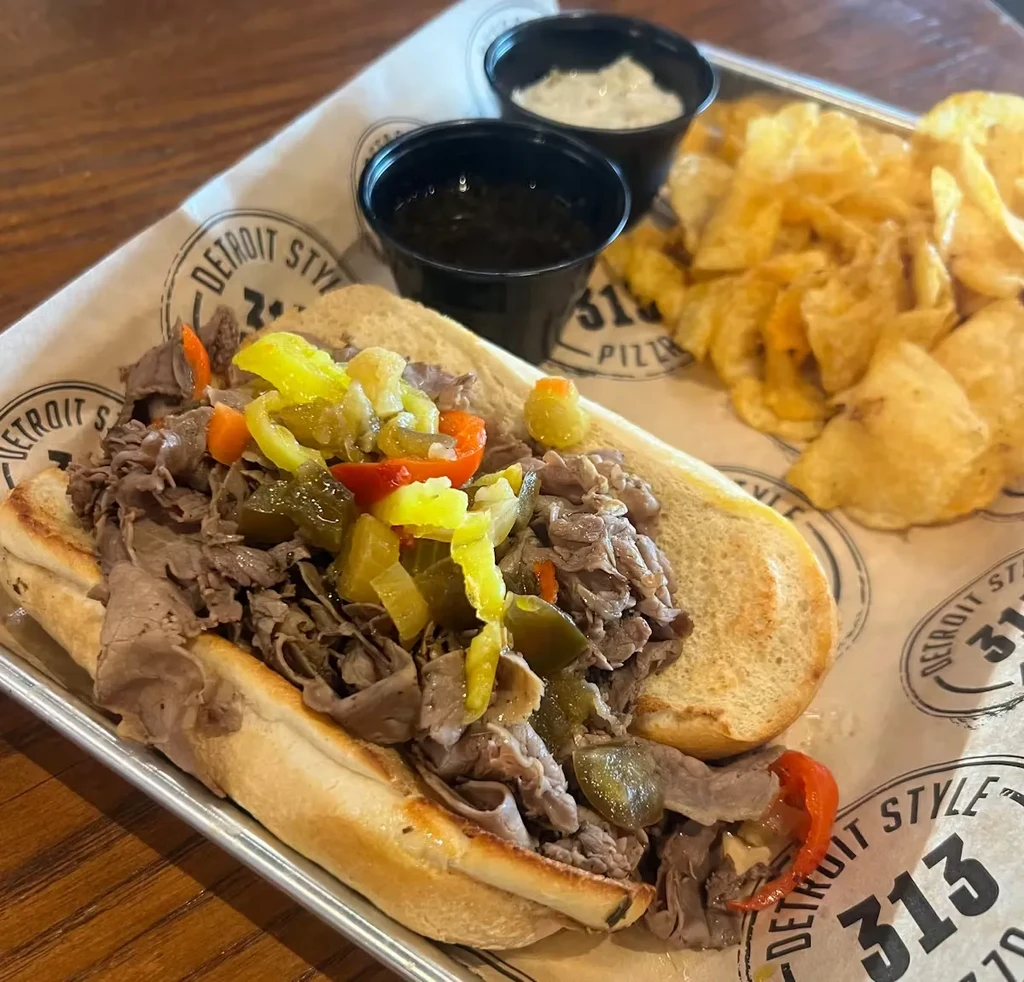 Roast beef hoagie with pickled vegetables, crinkle chips, and two dips.