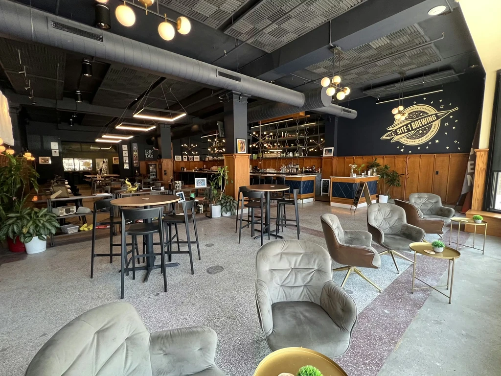 SITE-1 BREWING interior: industrial design, diverse seating, bar, and plants.