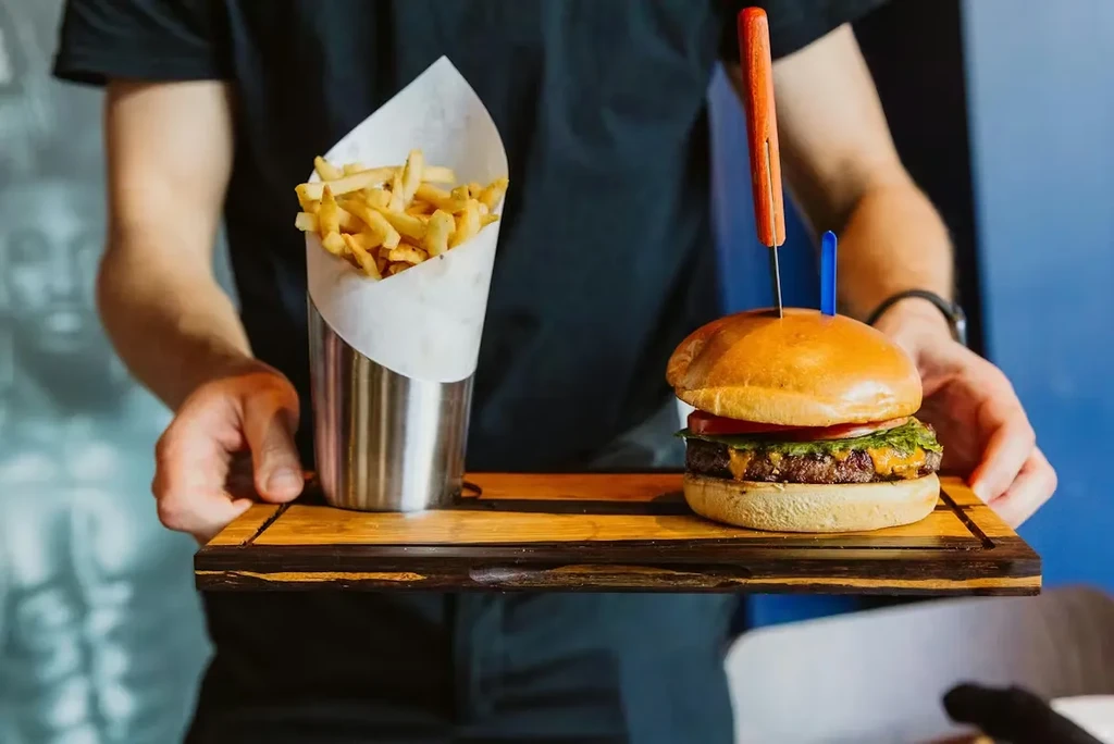 Hands holding a wooden tray with a gourmet burger and fries.
