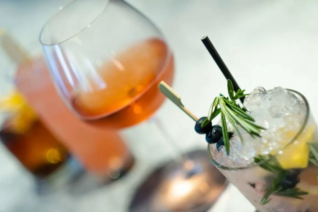 Close-up of two drinks, clear with rosemary and an orange beverage.