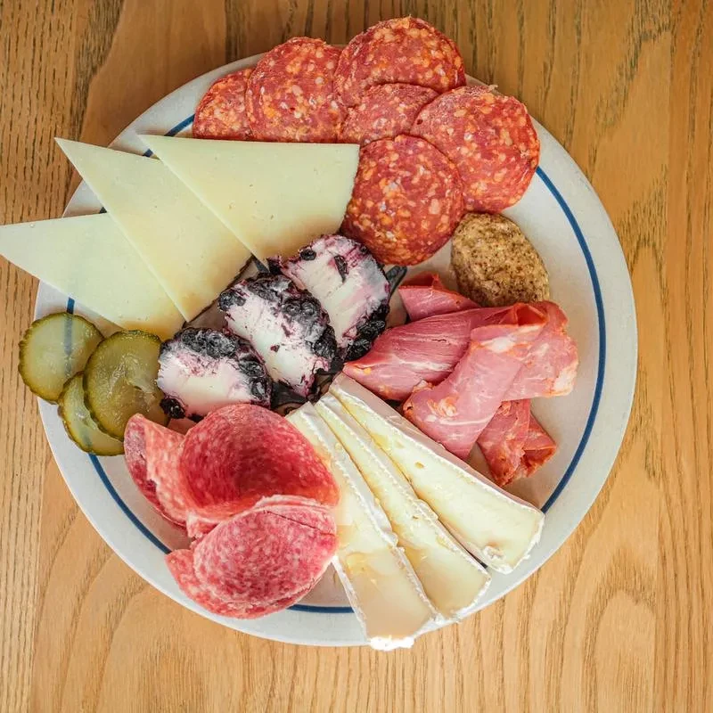 Close-up of a charcuterie board with cured meats, cheeses, and gherkins.