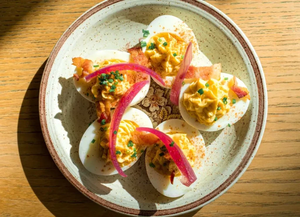 Five deviled eggs with chives, bacon, red onion on a speckled plate.