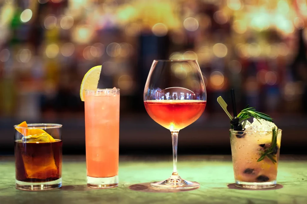 Four varied alcoholic drinks on a bar with blurred background.