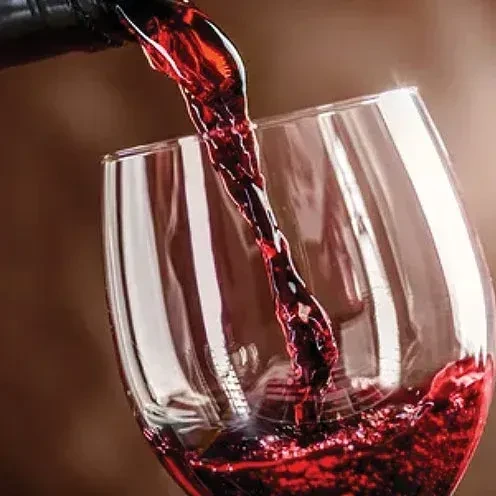Dark red wine streams from bottle into a tilted clear glass.