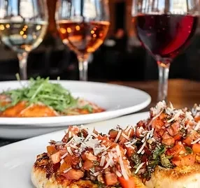 Close-up of grilled chicken, pasta, and three wines in a restaurant.