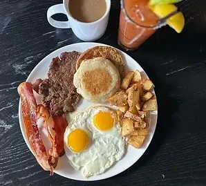 Overhead full breakfast spread: eggs, bacon, sausage, potatoes, coffee, Bloody Mary.