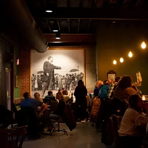 Lively, dimly lit restaurant interior with a historical mural and patrons.