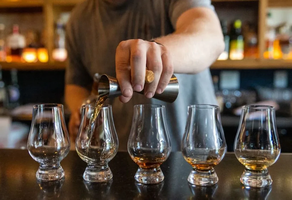Bartender's hands pour whiskey from jigger into tulip-shaped glass.