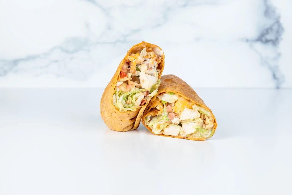 Halved chicken wrap filled with lettuce, tomatoes, and chicken on white.