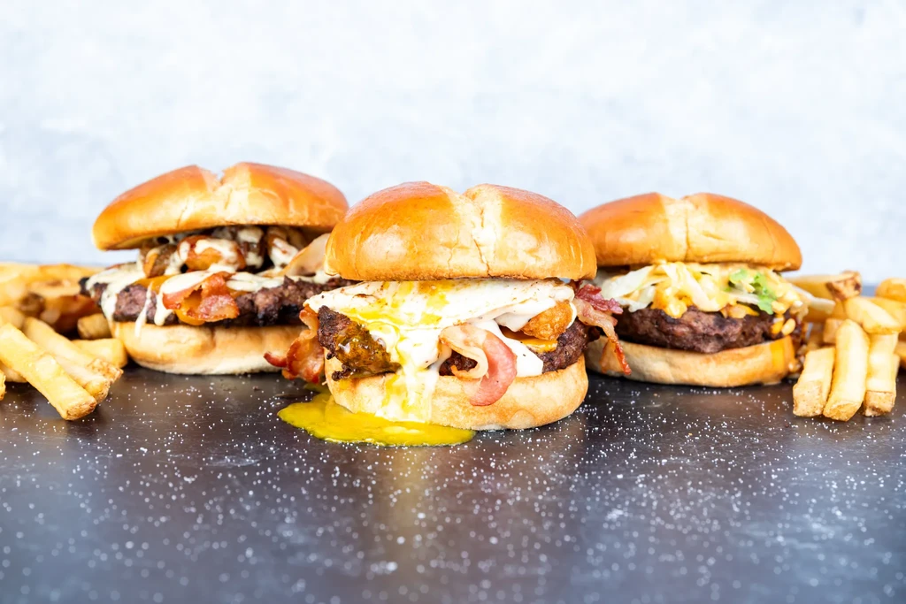 Three gourmet burgers with diverse toppings, flanked by french fries.