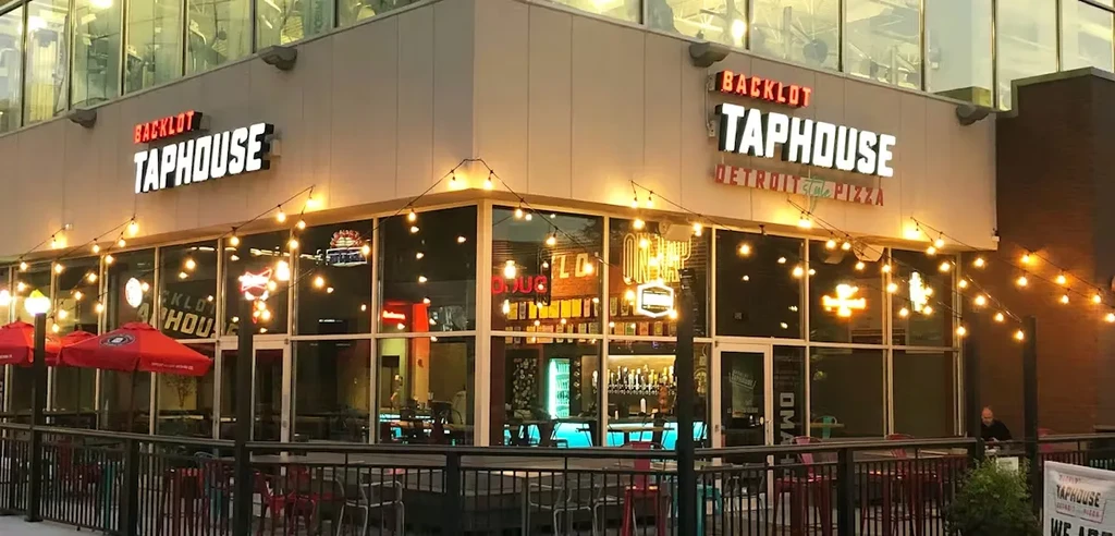 Modern Backlot Taphouse exterior at dusk with string lights and patio.