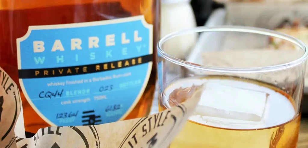 Barrell Whiskey bottle, glass with ice cube, label visible.