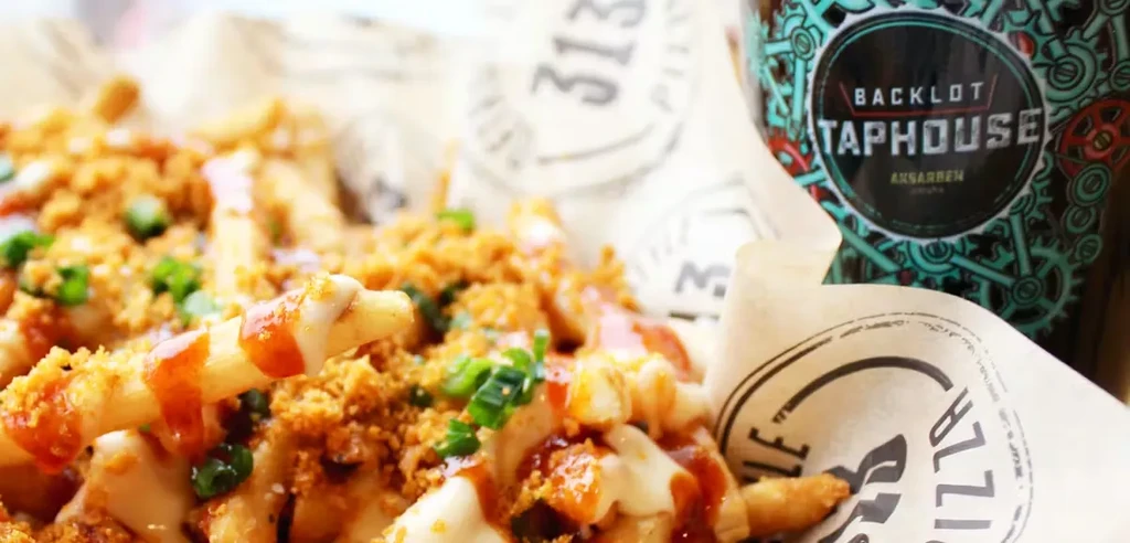 Golden loaded fries with sauces, green onions, and a branded bottle.