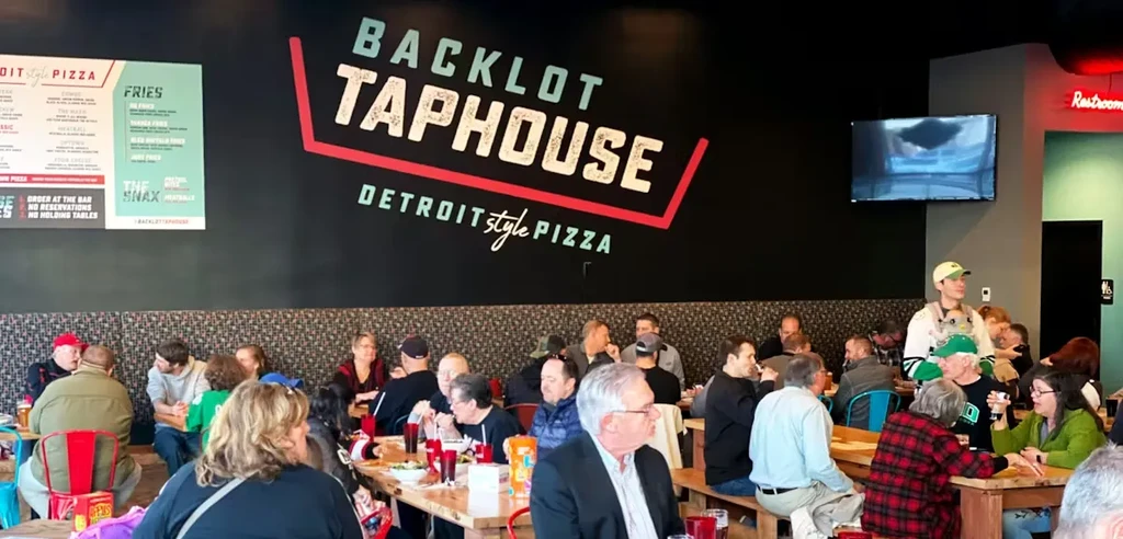 Patrons fill the bustling Backlot Taphouse, eating Detroit-style pizza.