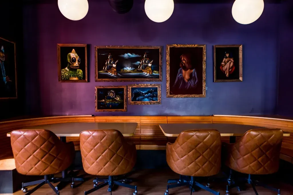 Curved banquette and swivel chairs before a purple-blue art gallery wall.