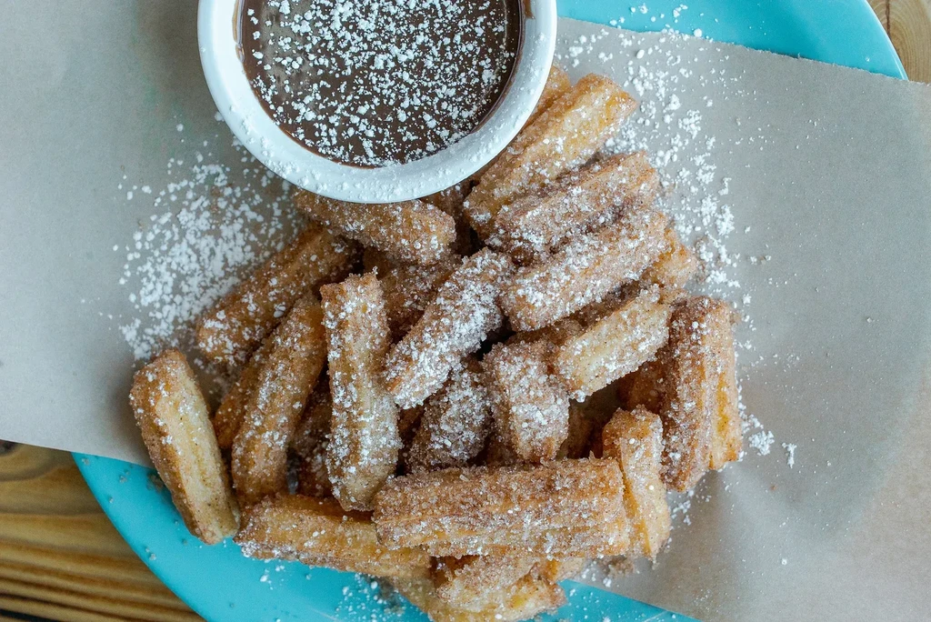 Close-up of golden churros with cinnamon, powdered sugar, and chocolate sauce.