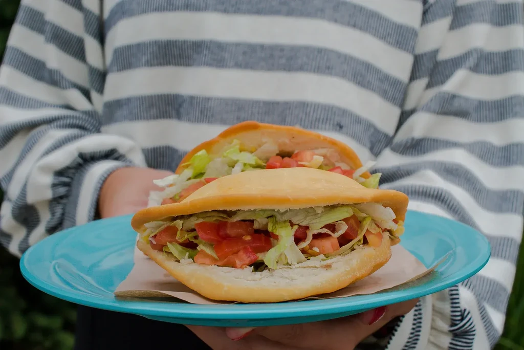Two puffy golden flatbreads stuffed with lettuce and tomatoes on plate.
