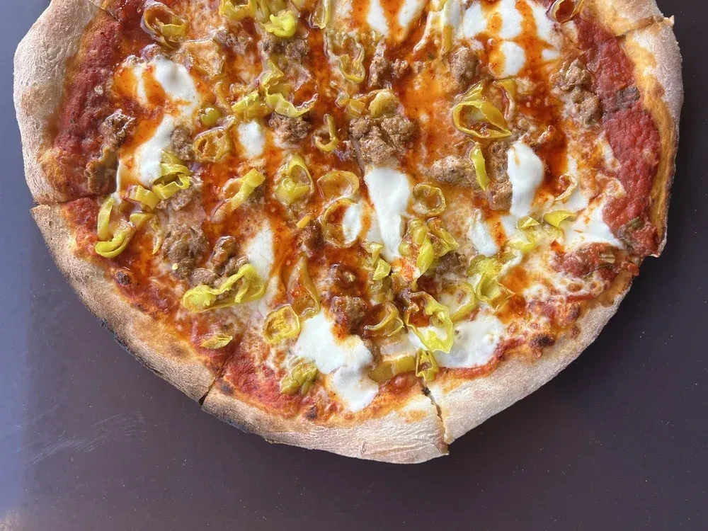Overhead: Sausage and pepper pizza with spicy drizzle, sliced.