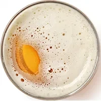 Top-down close-up of golden-amber drink with thick white foam.