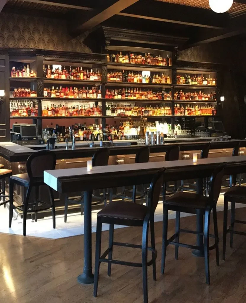 Sophisticated bar with backlit liquor bottles, counter, and high-top table.
