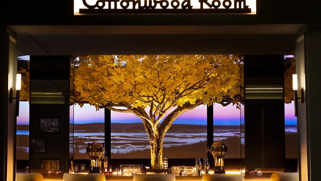 Cottonwood Room bar interior with glowing golden tree and sunset landscape.