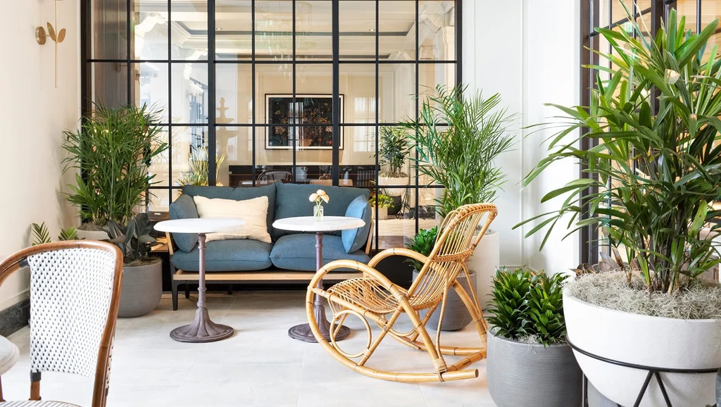 Indoor seating area with teal sofa, marble tables, wicker chair, and plants.