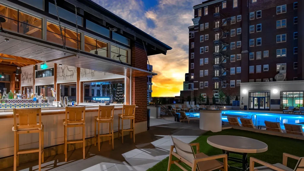 Dusk view of an outdoor bar, illuminated pool, and vibrant sunset.