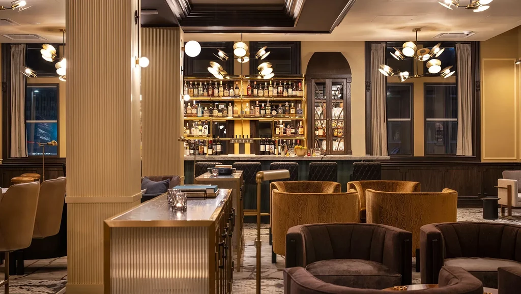 Interior view of a modern, well-stocked bar with plush armchairs.