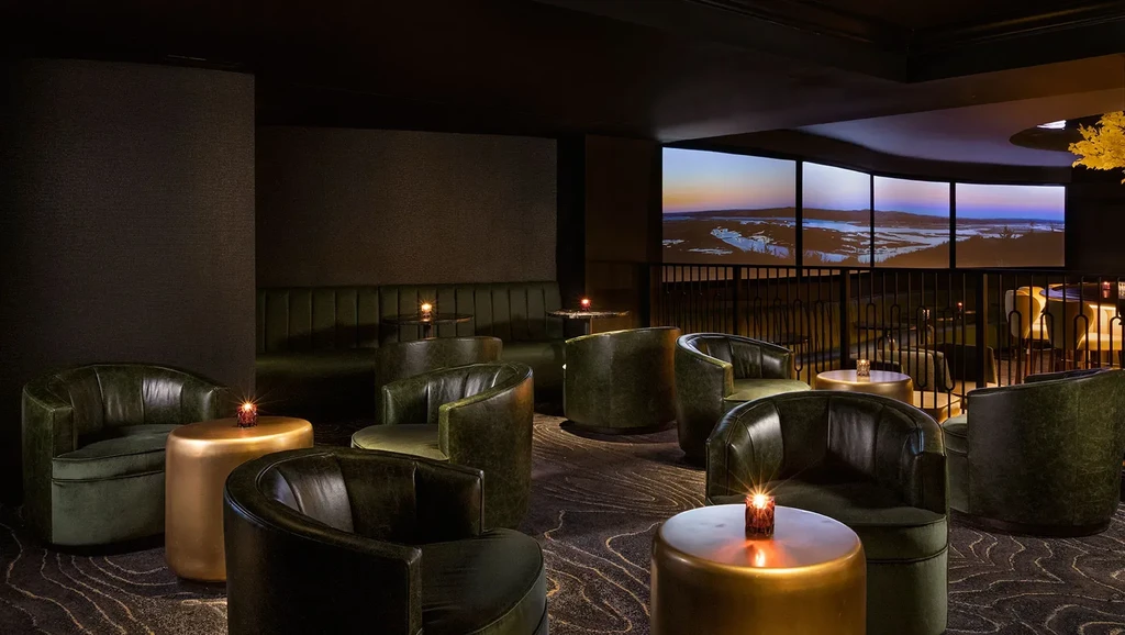 Dimly lit lounge with green armchairs, candles, and twilight landscape view.